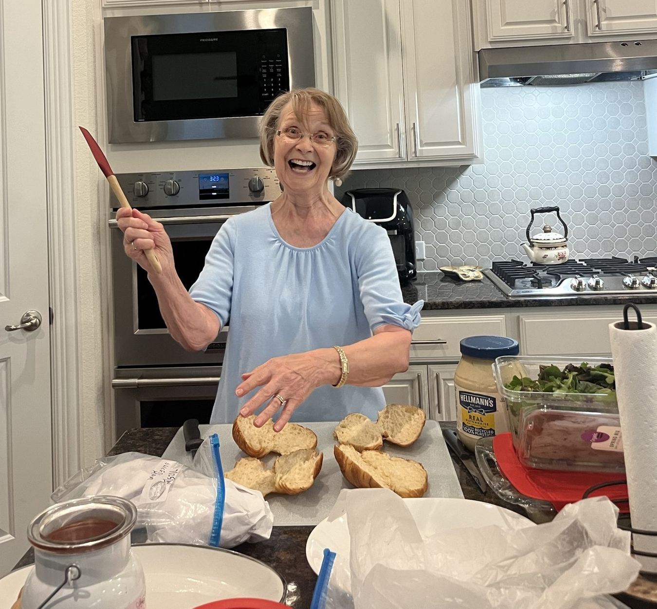 Nana Donna laughing in her kitchen, holding a spatula over slices of fresh bread