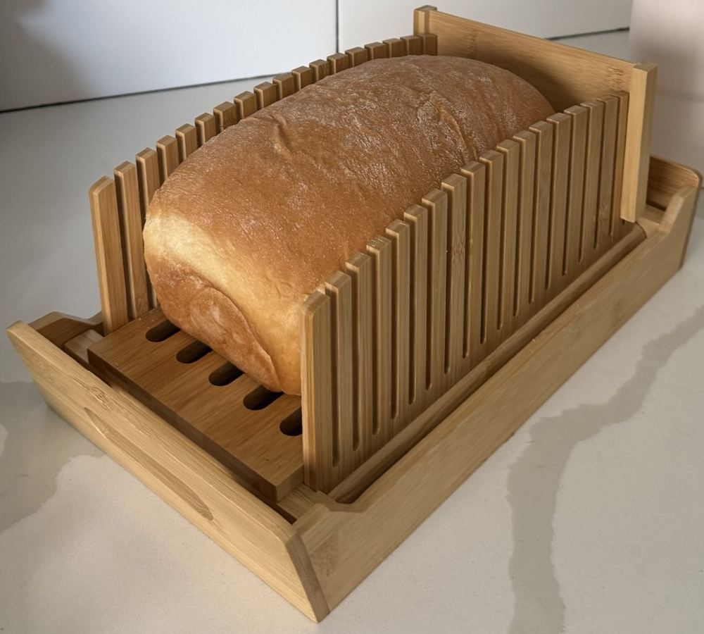 Whole loaf of white bread sitting in a bamboo bread slicing guide
