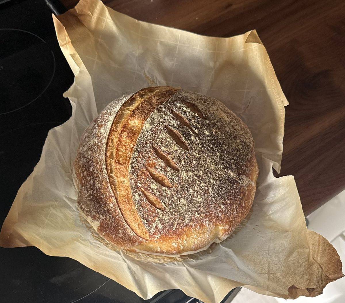 Round country loaf sourdough boule with a scored, flour-dusted crust, resting on crinkled parchment