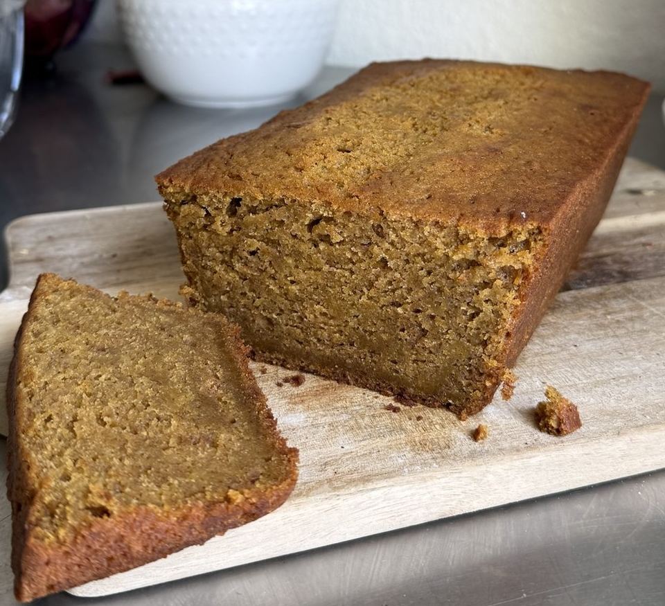 Moist pumpkin bread loaf on a wooden board with a thick slice cut and laid in front