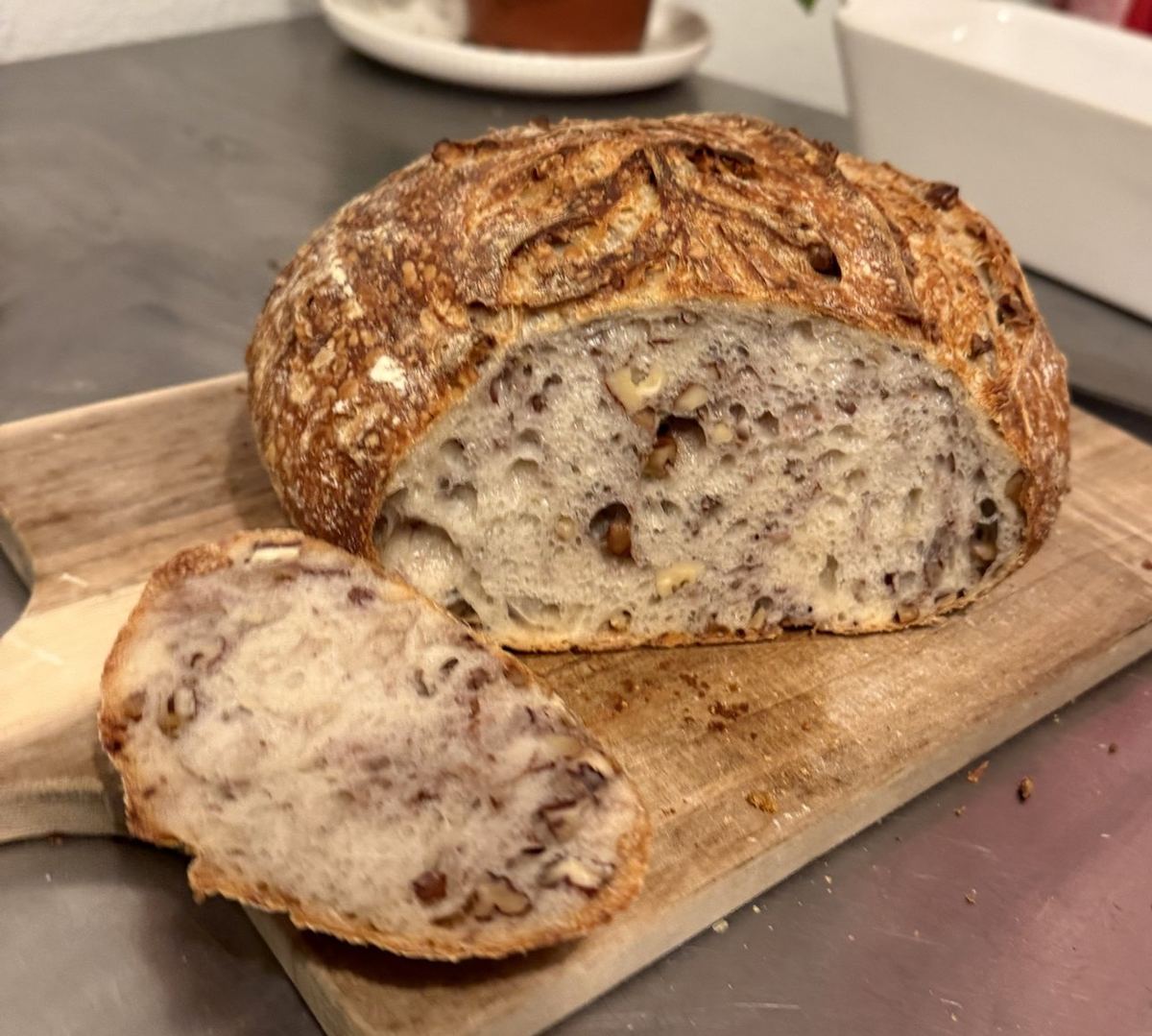 Close view of walnut pecan sourdough cut in half, walnuts and pecans speckled through the crumb, with a thick slice laid in front on the board