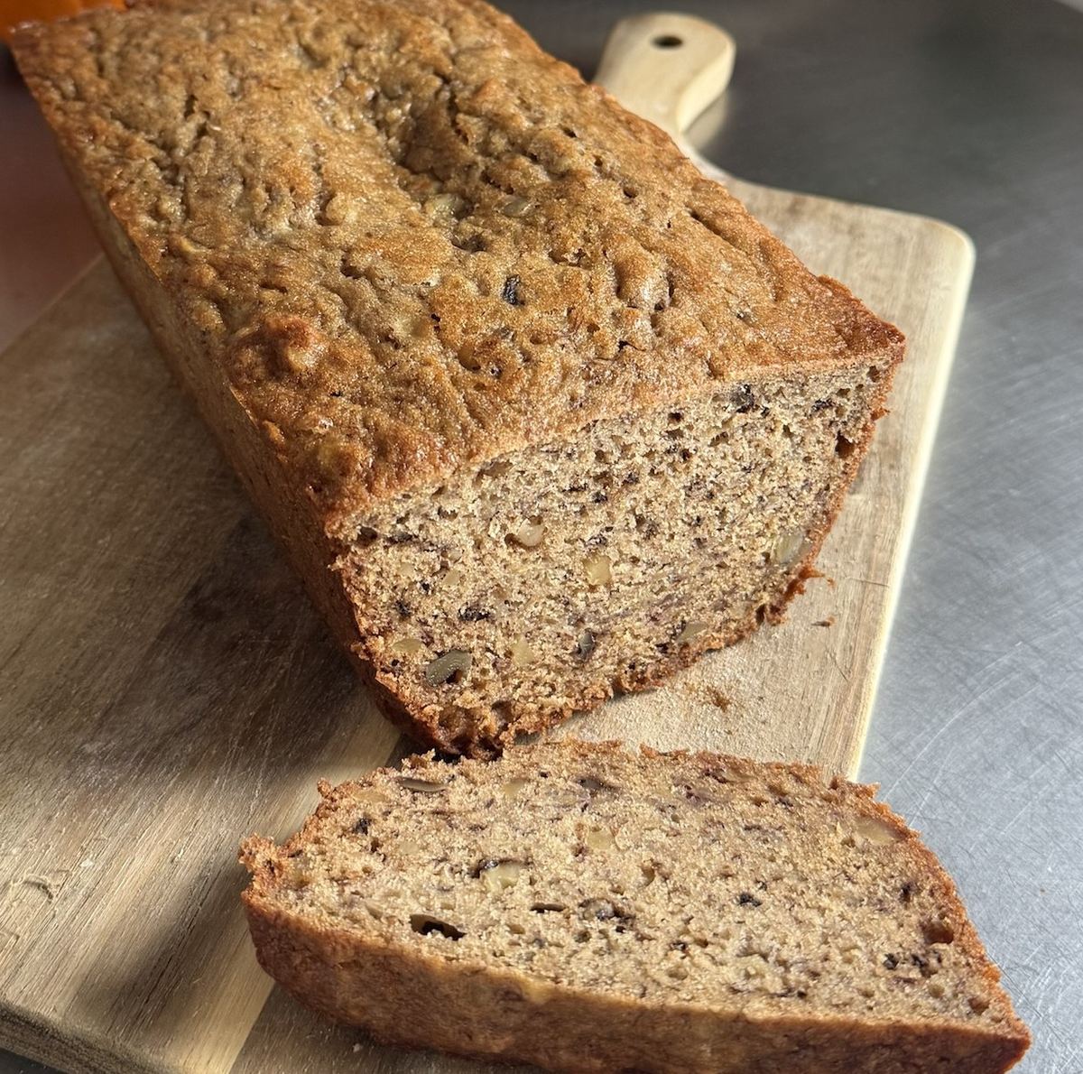Walnut banana bread loaf on a wooden board with a thick slice cut from one end, walnuts speckled through the golden crumb