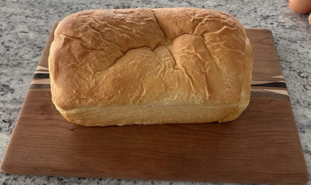 Tall golden loaf of homemade white bread on a wooden cutting board