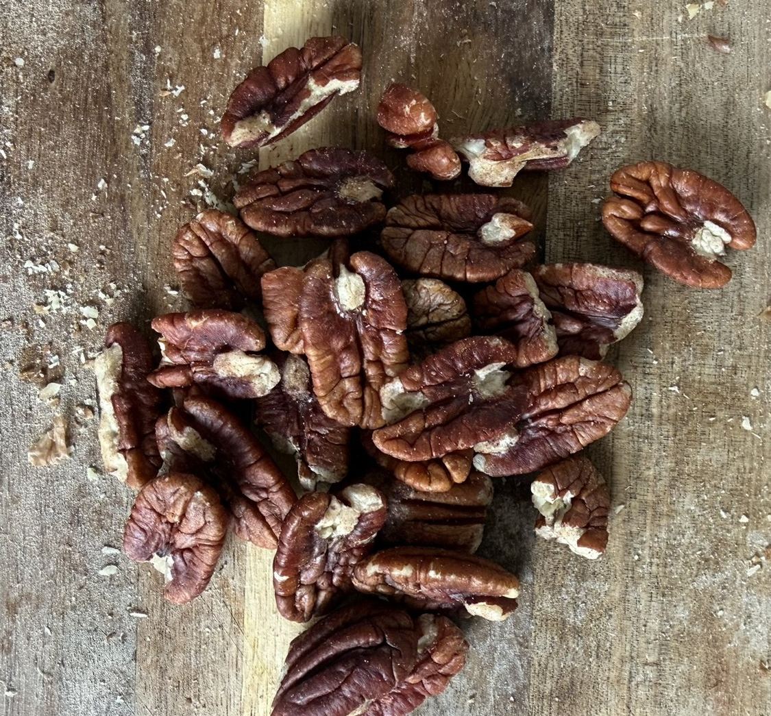 Pile of pecan halves on a wooden cutting board
