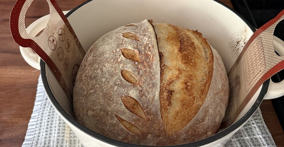 Sourdough loaf inside an enameled cast-iron Dutch oven on a silicone baking sling