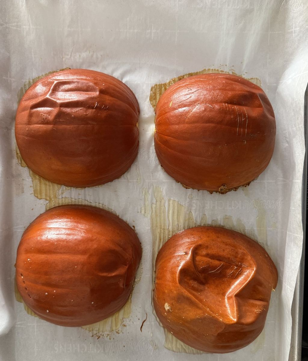 Four pie pumpkin halves roasted cut-side down on a parchment-lined tray